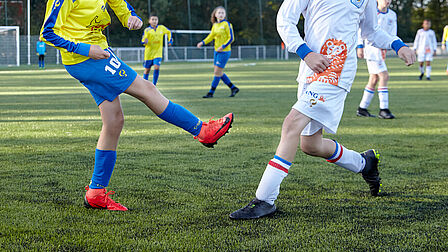 Duel op het gras tussen 2 voetballers van verschillende clubs
